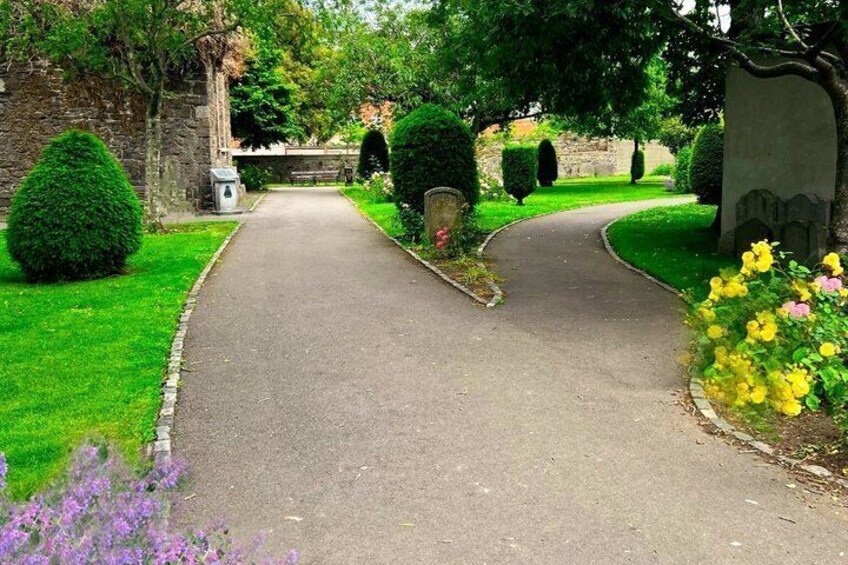 A paved pathway curving through a well-maintained garden with neatly trimmed hedges and flowering plants. 5