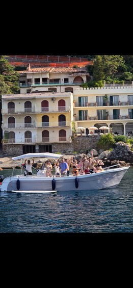 A boat with people on it, docked near a building with multiple balconies. 1