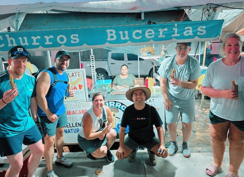 A group of people posing in front of a churros and bucerias food stall. 1
