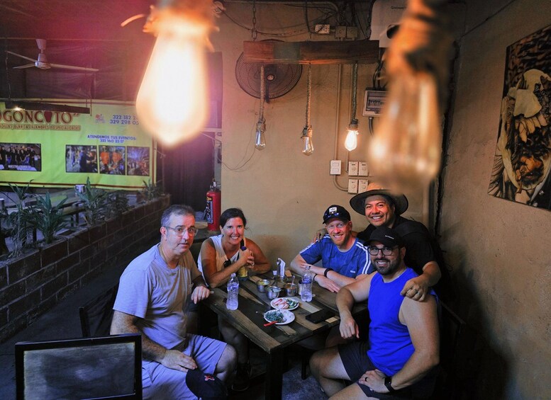 A group of people sitting at a wooden table in a restaurant with hanging light bulbs. 3