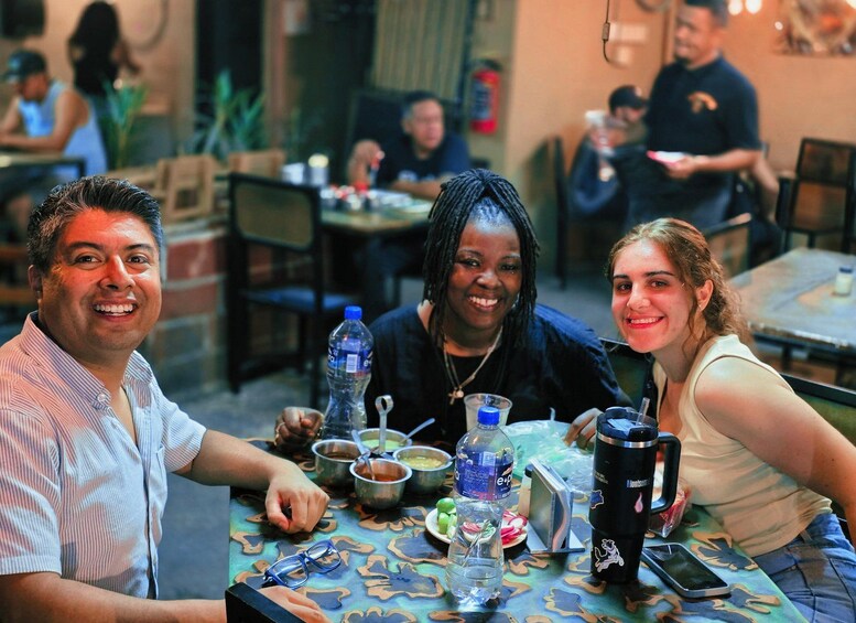 A group of people sitting at a table with various items like bottles, glasses, and a thermos. 4