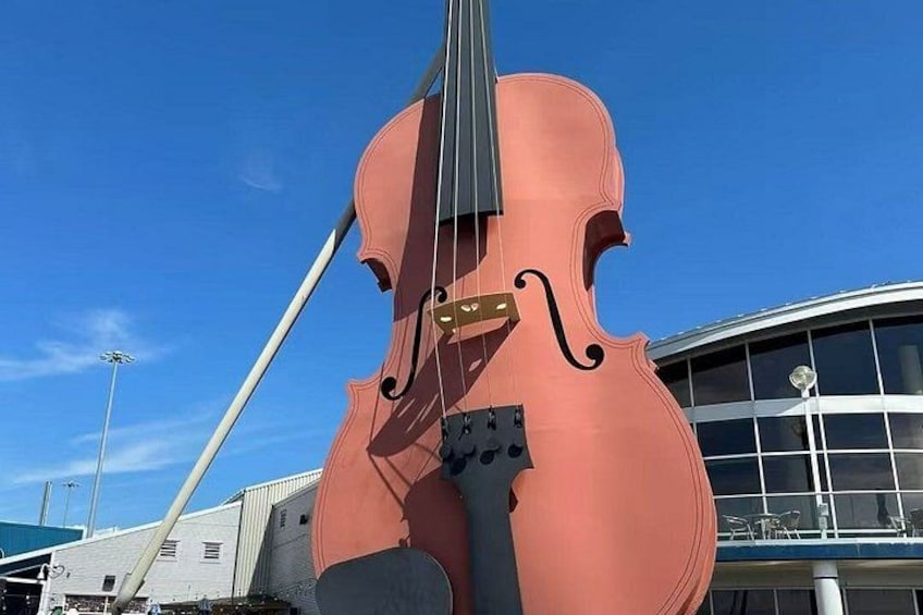 A large, pink violin sculpture outdoors with a modern building in the background. 5