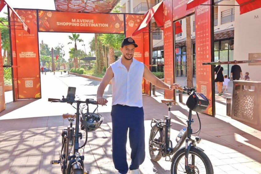 A person standing next to a bicycle in front of a shopping destination sign. 1