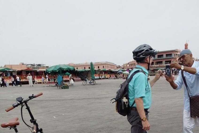 A busy outdoor market with people walking, a bicycle, and a man taking a photo. 3