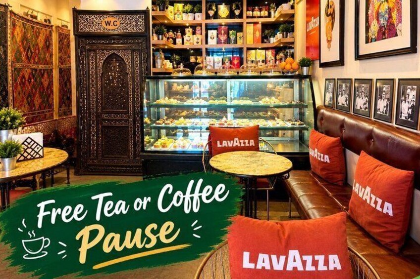 A cozy cafe interior with a 'Free Tea or Coffee Pause' sign, a display case with pastries, and a 'Lavazza' branded couch. 2