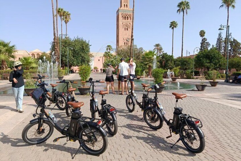 Bicycles parked in a plaza with palm trees and a tower in the background. 4