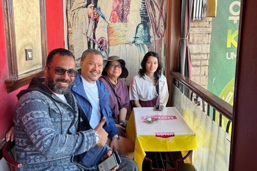 A group of people seated at a table with a yellow tablecloth, a mural on the wall, and a red door in the background. 2