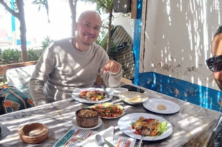A person sitting at an outdoor table with plates of food, a bowl, and a spoon. 3