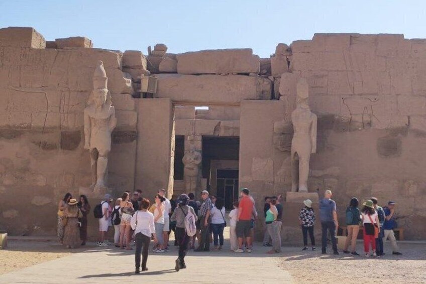 A group of tourists at an ancient Egyptian temple entrance with large statues and hieroglyphics. 5