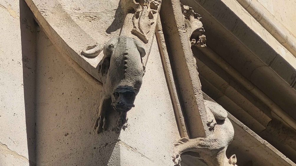 A stone gargoyle with a pointed nose and a carved face, attached to a building's corner. 4