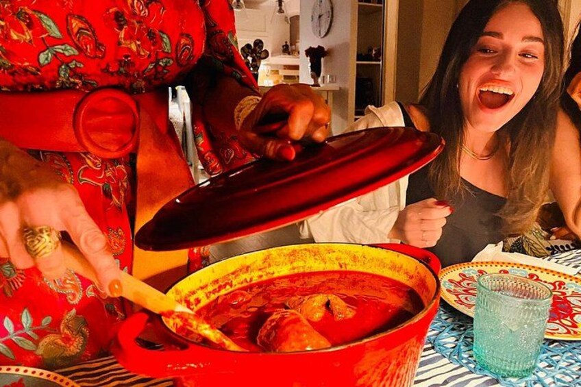 A person holding a red pot with a lid, a glass of water, and a patterned plate on a table. 2