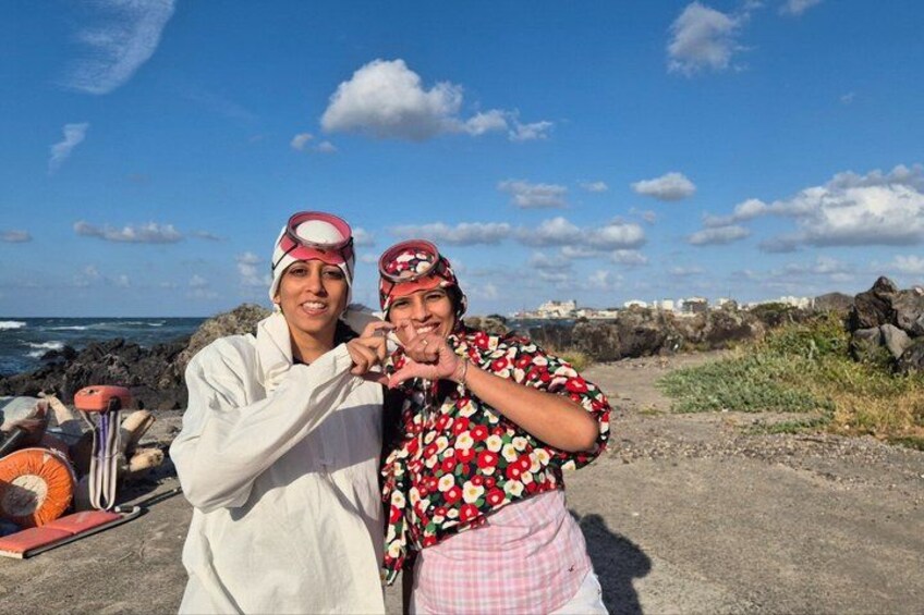 Two people making a heart shape with their hands, standing on a rocky shore with the ocean in the background. 4