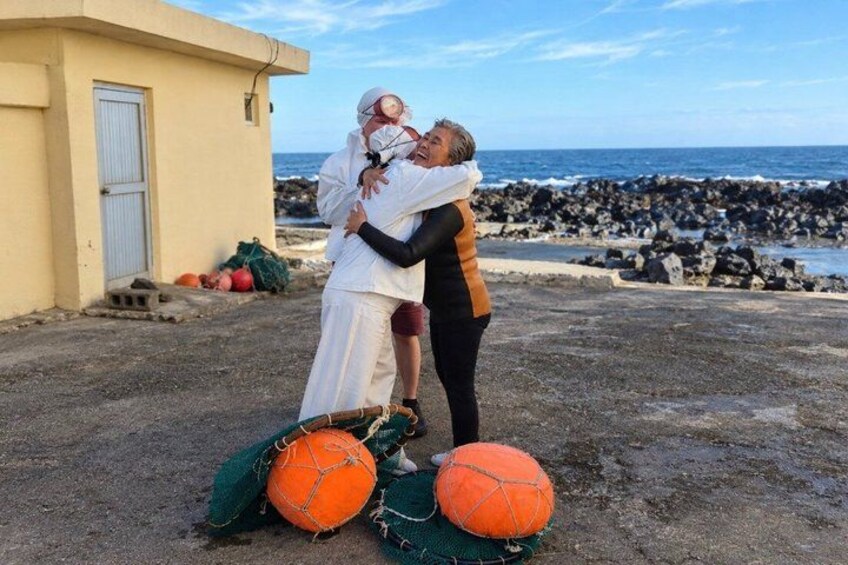 Two people embracing near a beach with rocks and a building in the background. 5