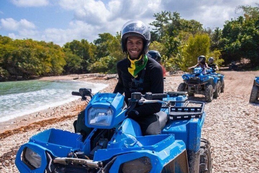 A person on a blue ATV on a beach with water and trees in the background. 3