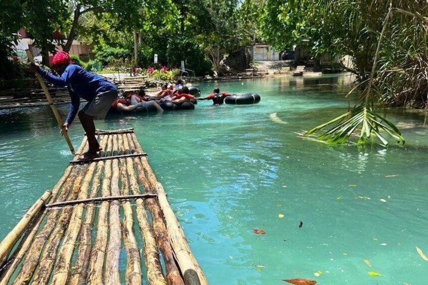 A person standing on a bamboo raft in a river, surrounded by greenery and other rafts. 1
