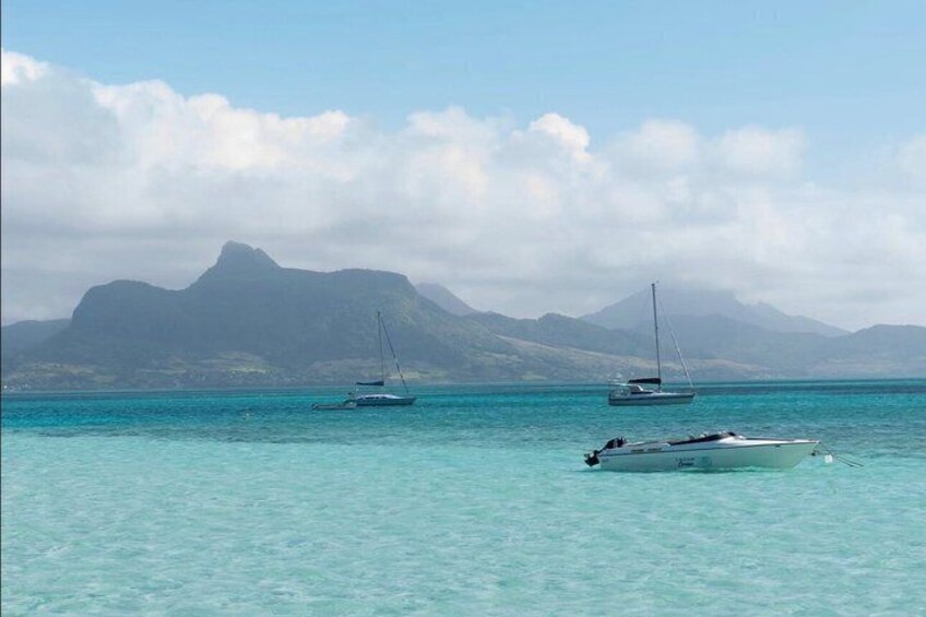 A calm sea with two sailboats and a motorboat, and a mountain range in the background. 3