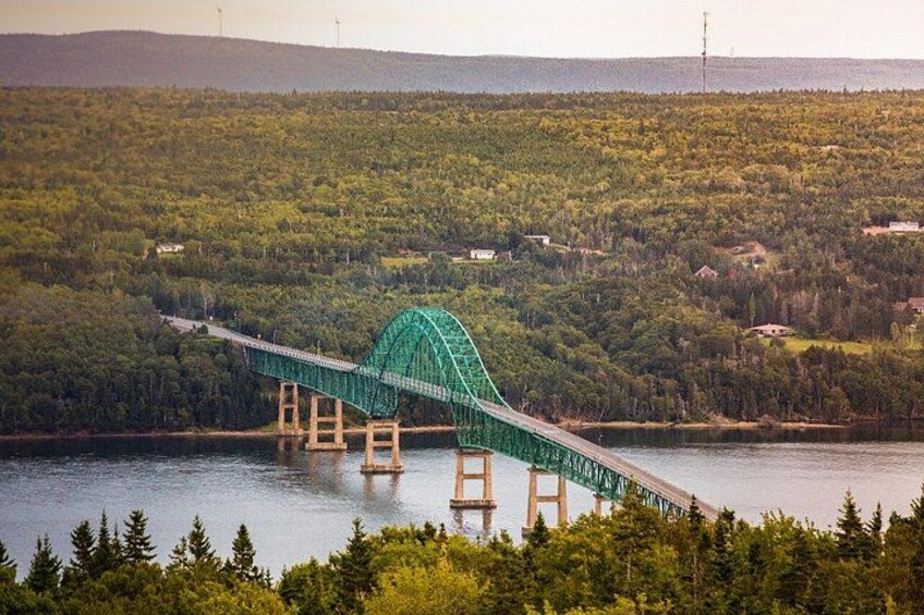 A green bridge over a body of water with forested hills in the background. 5
