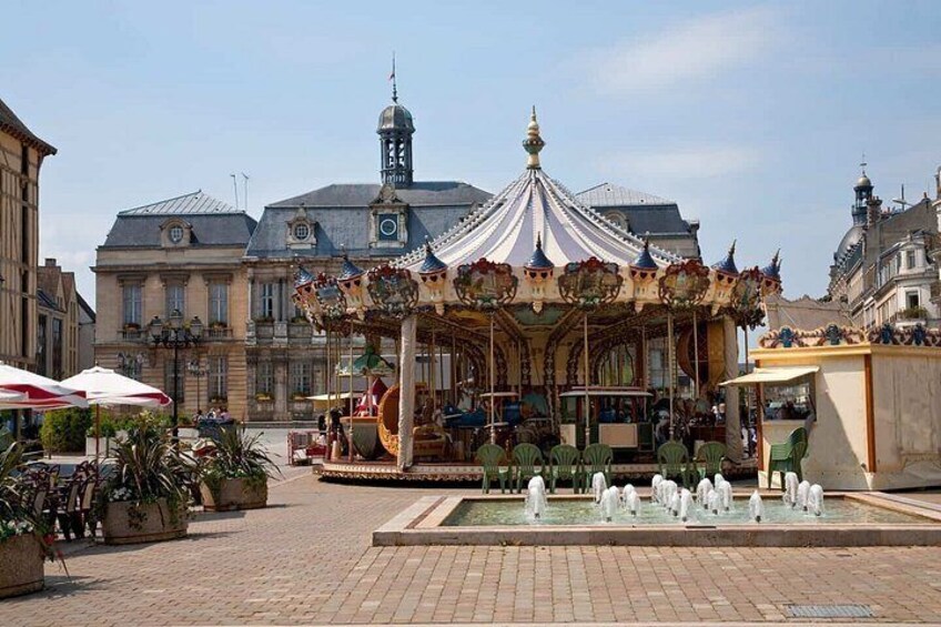 A carousel in a public square with surrounding buildings and a fountain. 5