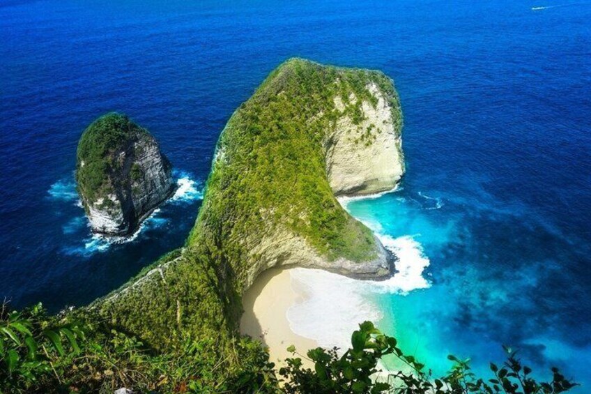 A coastal landscape with a prominent rock formation, a sandy beach, and clear blue waters. 1