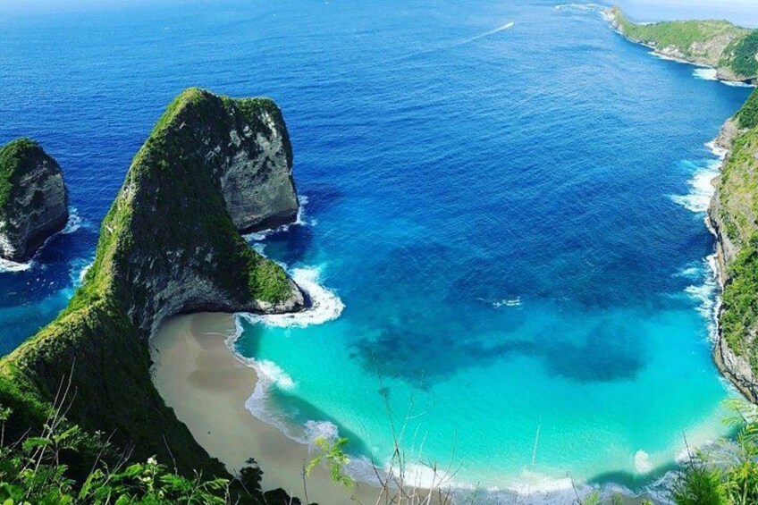 A coastal landscape with a clear blue sea, a sandy beach, and green cliffs. 2