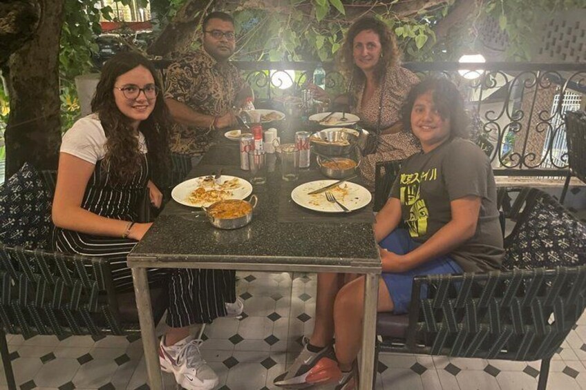 Three people dining at an outdoor table with plates of food and drinks. 5
