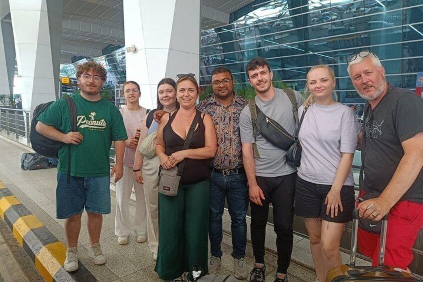 A group of people standing in an airport terminal with a modern glass building in the background. 4