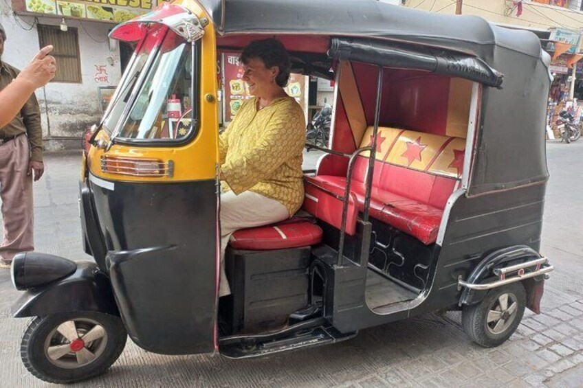 A yellow auto-rickshaw with red seats and a woman sitting inside. 1