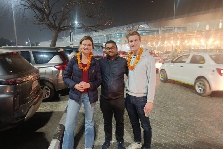 Three people standing in a parking lot at night with cars parked around them. 3