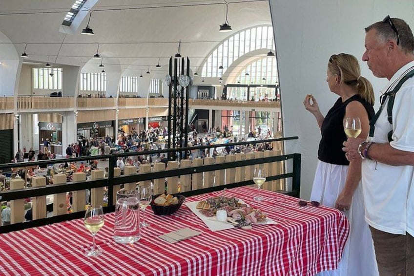 A dining area with a red and white checkered tablecloth, a clock, and a view of a busy indoor space with people and tables. 1