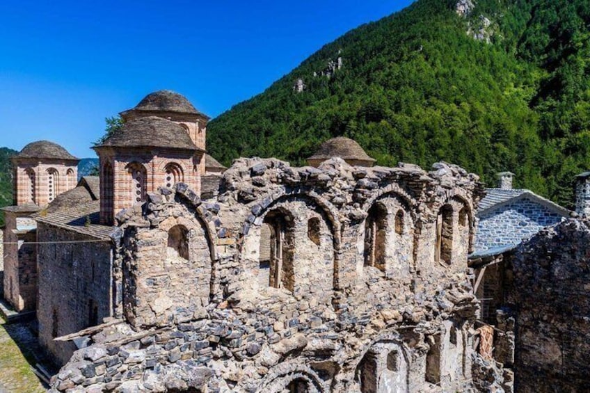 Ancient stone ruins with domed structures and arches, set against a backdrop of lush green mountains. 4