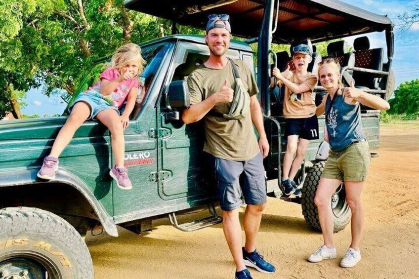 A family with a child and two adults standing in front of a green off-road vehicle. 2