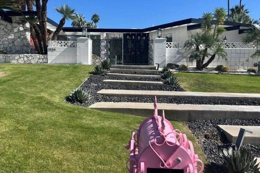 A modern house with a stone facade, a well-manicured lawn, and a pink lawnmower in the foreground. 4
