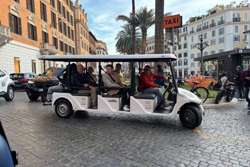 A white golf cart with passengers on a cobblestone street. 2