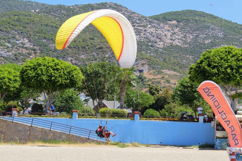 A person paragliding with a yellow and white parachute, a blue wall, and a mountainous landscape in the background. 3