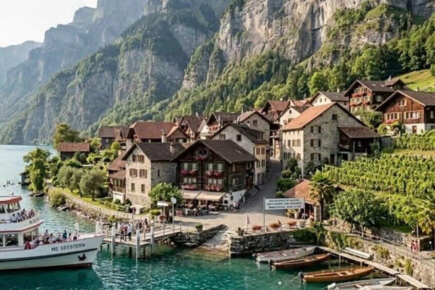 A lakeside village with traditional buildings, boats docked at the pier, and steep cliffs in the background. 2