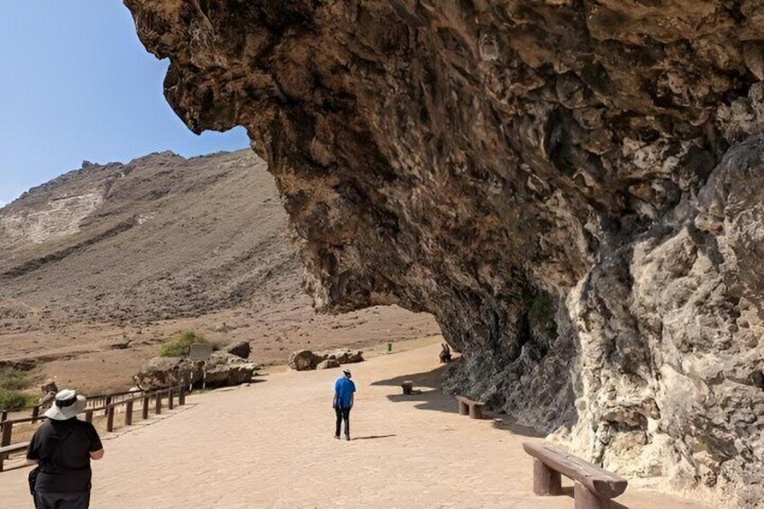 A rocky cave entrance, a sandy path, and a distant hilly landscape. 3