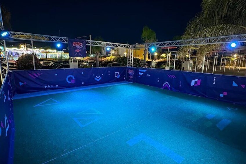 A nighttime swimming pool with geometric patterns on the deck, surrounded by a metal fence and palm trees. 2