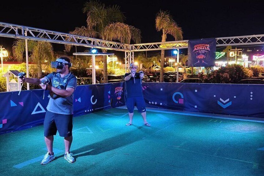 Two people wearing VR headsets on a stage with a banner reading 'Adventure Arena' in the background. 4