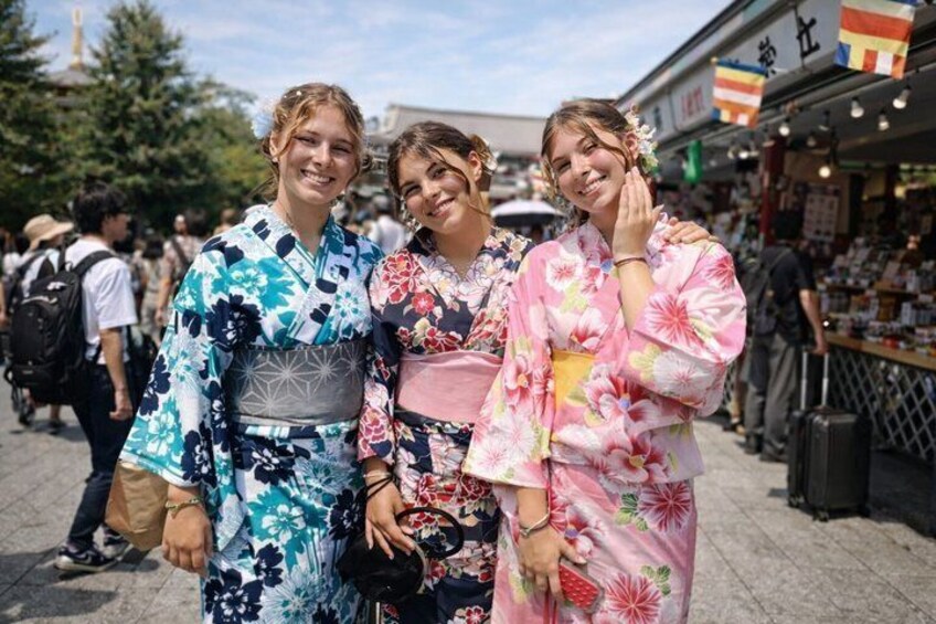 Three individuals wearing traditional Japanese kimonos in an outdoor market setting. 1