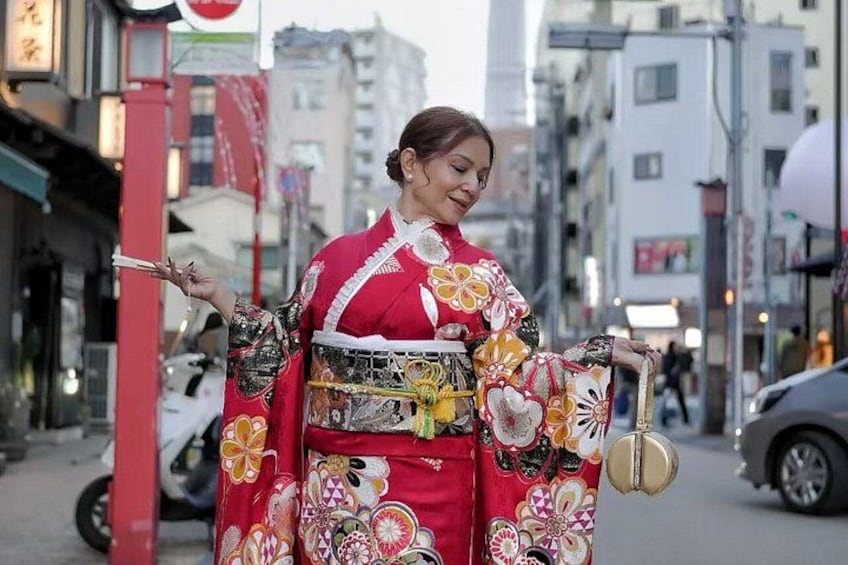A person in traditional attire holding a fan and a decorative item on a city street. 5