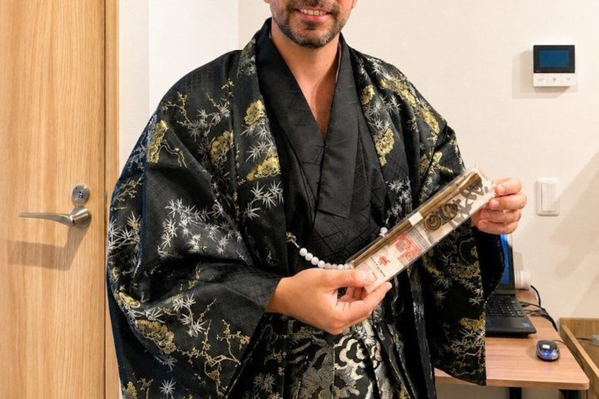 A person in a black kimono with gold patterns holding a clear object with a red label. 3