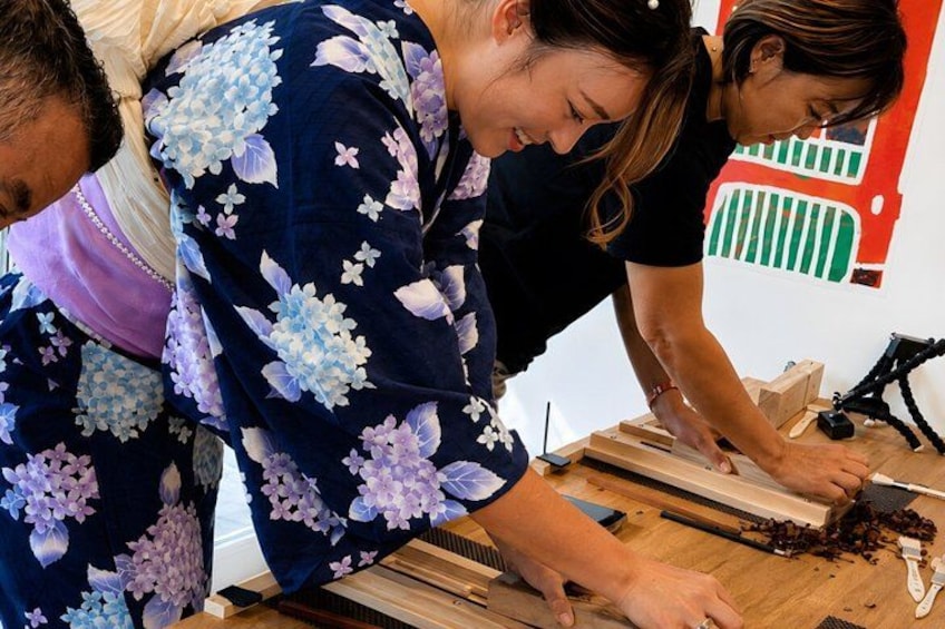 People working with a wooden board and a tool, possibly carving or cutting. 2