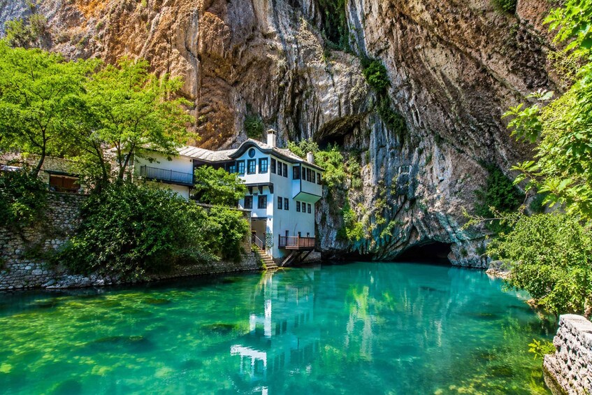 A house by a clear turquoise lake with a rocky cliff backdrop. 2