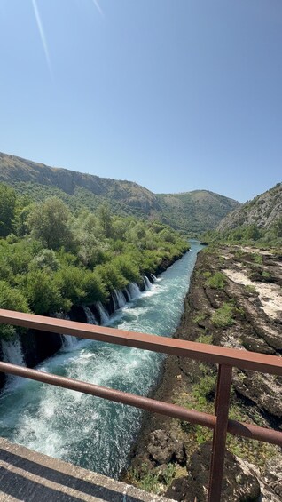 A river flowing through a mountainous landscape with lush greenery and a bridge in the foreground. 3