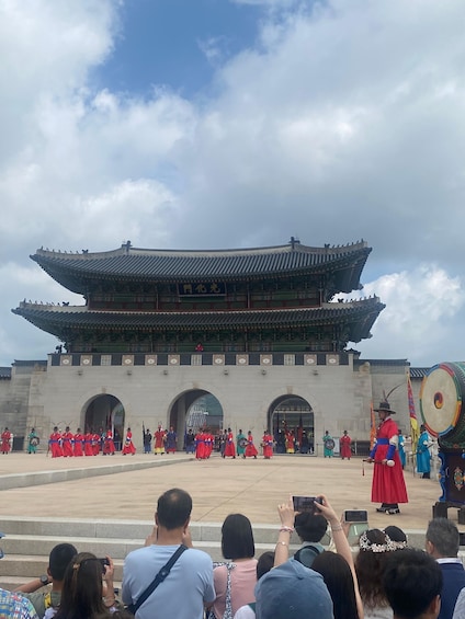 Perinteinen korealainen palatsi, jonka edessä punaisiin hanbok-pukuihin pukeutunut ryhmä ihmisiä esiintyy. 1