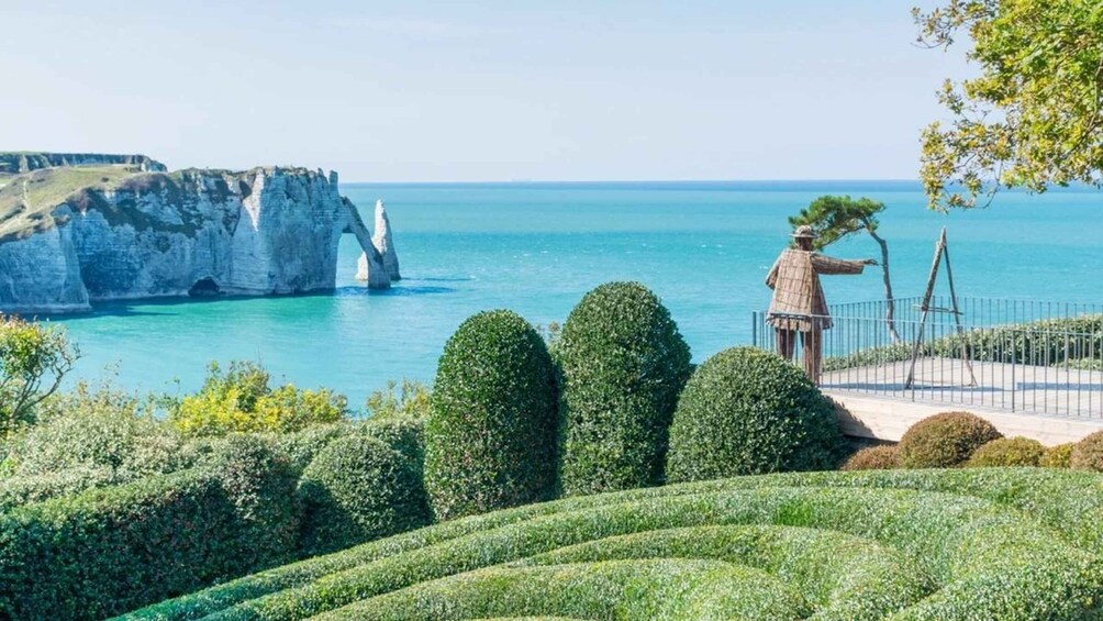 A coastal landscape with white cliffs, a statue, and manicured hedges. 2