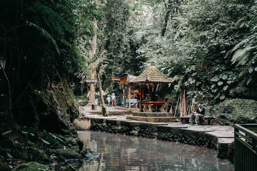 A tranquil river with a small wooden structure and people around it. 5