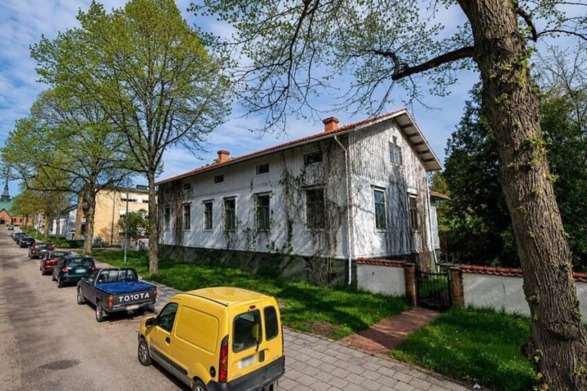 A street with parked cars, a yellow van, and a weathered building with a red roof. 4