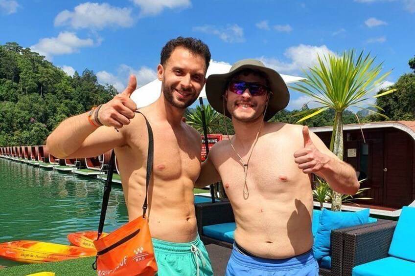 Two people giving thumbs up by a pool with lounge chairs and palm trees in the background. 2