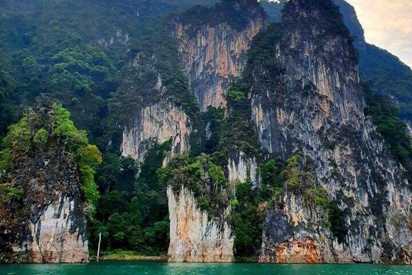 A coastal landscape with towering limestone cliffs and dense green foliage. 4